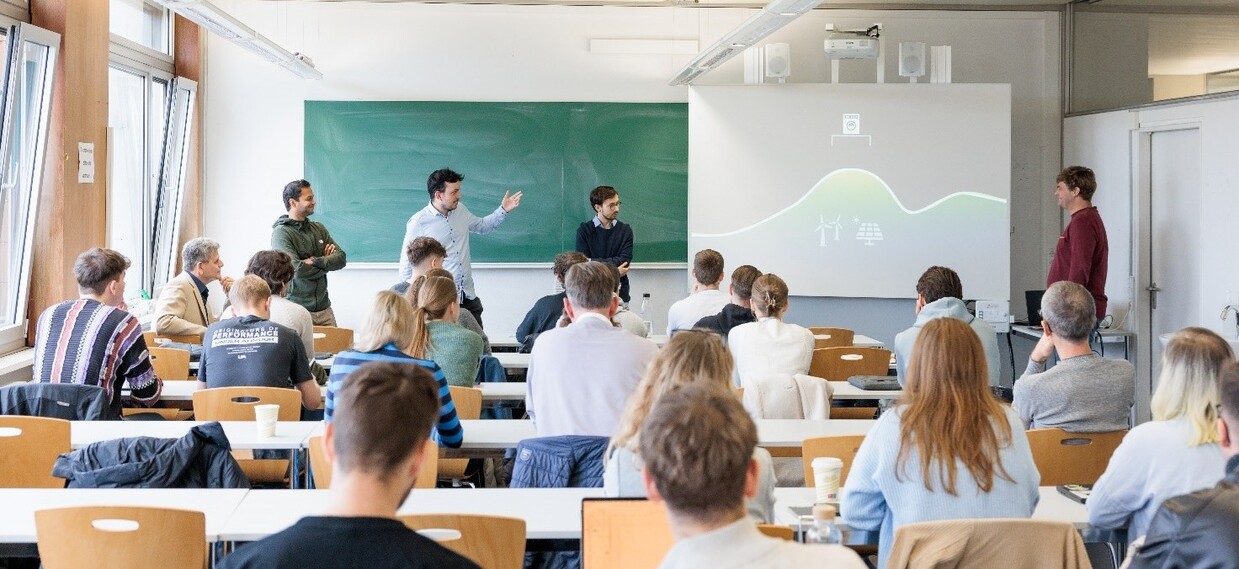 Gruppe von Studierenden in einem Hörsaal, vorne Präsentation und Tafel.